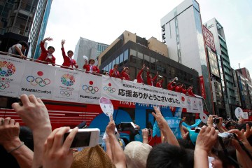 People cheer as Japan's national women's soccer team wearing silver medals wave atop an open-top bus parade in Tokyo